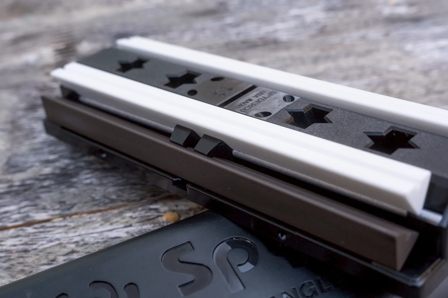 Close-up of the Sharpmaker base with its star-shaped keyed rod slots, white and brown ceramic rods laid across it