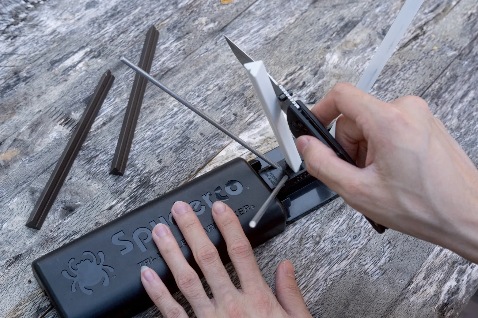 Hands drawing a blade down the white rods of a Sharpmaker, spare brown rods and a safety rod beside it